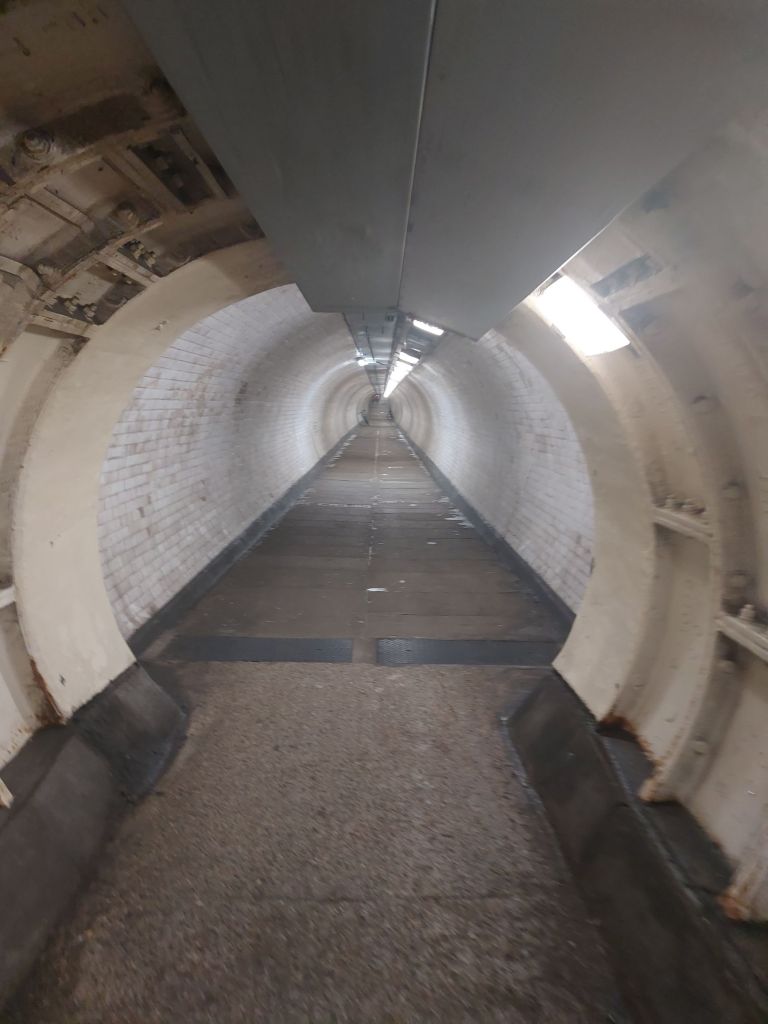 a long tunnel with a bit closer to the photographer that is distinct in construction out of metal compared to the brick and tile of the rest of the tunnel